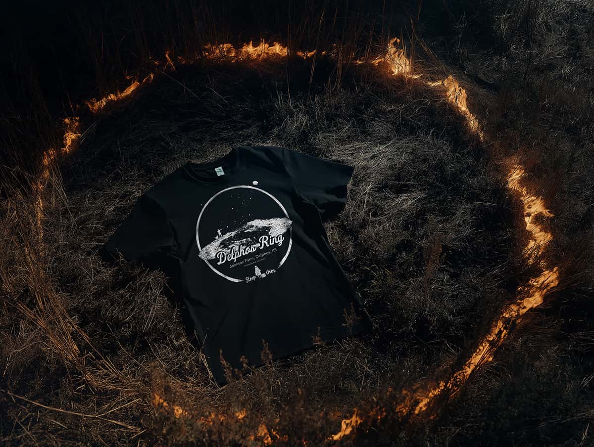 Delphos Ring t-shirt by SleepOver Clothing displayed inside a burning circle in a dark, haunted field at night.