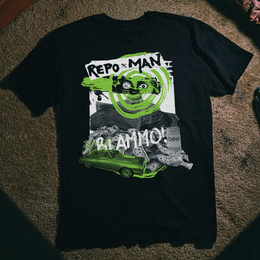 A black short-sleeve graphic T-shirt laid flat on a textured brown carpet. The shirt features a large distressed graphic with the text 'REPO x MAN' and '41 AMMO!' in white, a green circular logo, a green car, and a grayscale collage background.