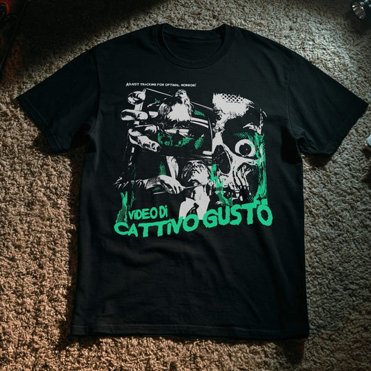 A black short-sleeve graphic t-shirt laid flat on a brown carpet. The shirt features a large, stylized graphic print in white and bright green, with the text 'VIDEO DI CATTIVO GUSTO' in green at the bottom.