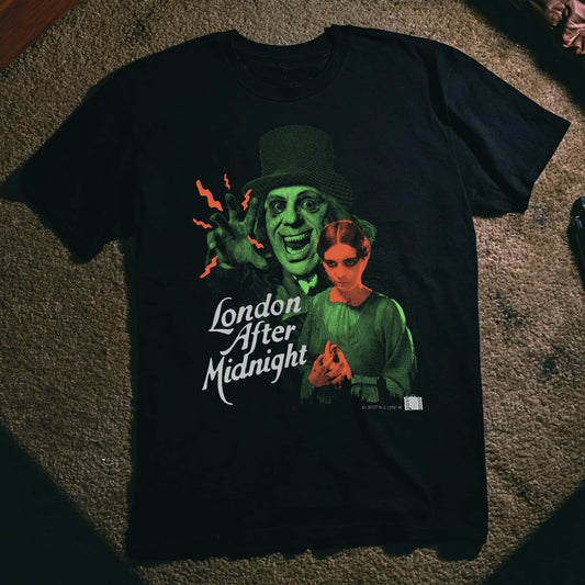 A black graphic t-shirt laid flat on a textured brown carpet. The shirt features a stylized green-toned illustration of a man in a top hat and a woman, with the text 'London After Midnight' in white script.