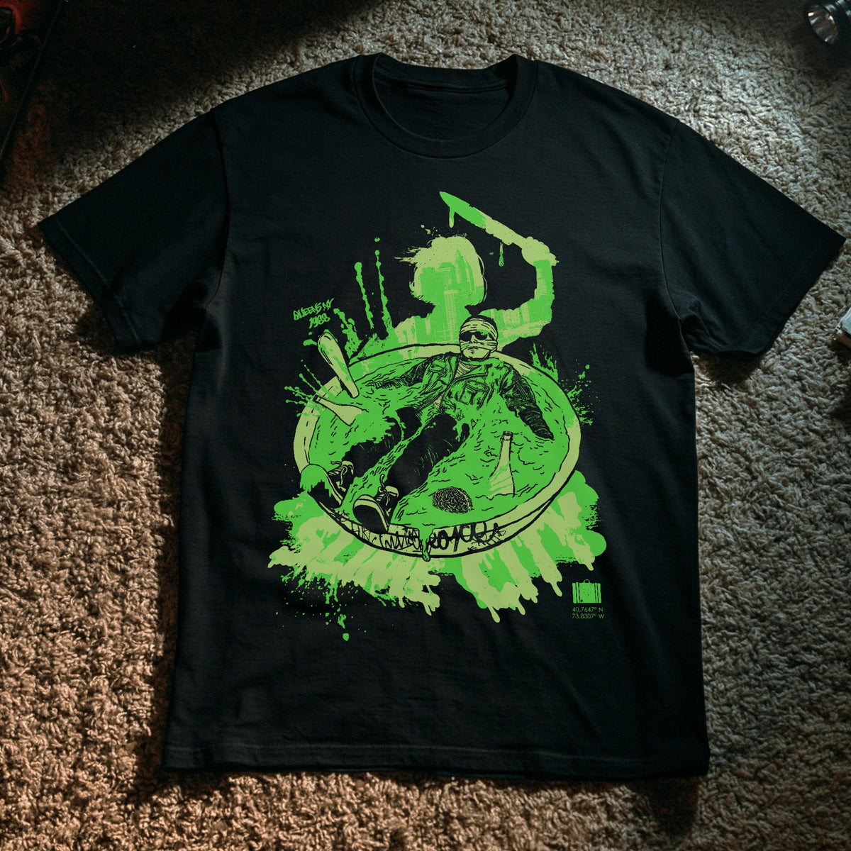 A black short-sleeve graphic t-shirt laid flat on a brown carpet. The shirt features a large neon green and white graphic print on the front depicting a character in a bowl with the word 'Slime City' and a small green Suitcase logo in the bottom right corner.