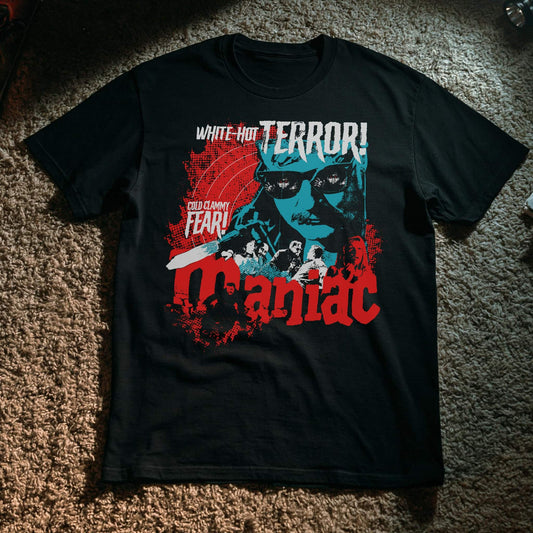 Black t-shirt with a vintage horror movie poster design in red, teal, and white for 'Maniac,' featuring a menacing man in sunglasses, a chainsaw, and a group of victims, with tagline text reading 'White-Hot Terror!' and 'Cold Clammy Fear!
