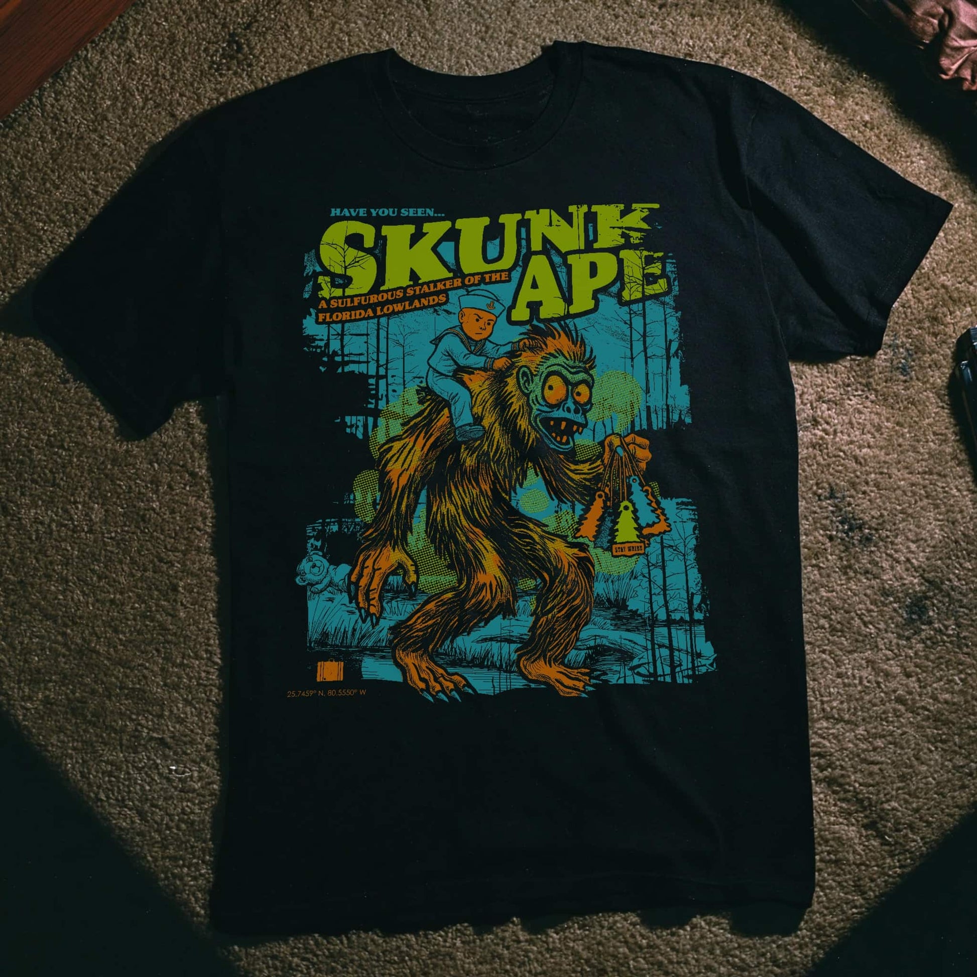 Skunk Ape graphic t-shirt featuring Florida's cryptid legend with a sailor boy riding on its back and a Robert the Doll cameo