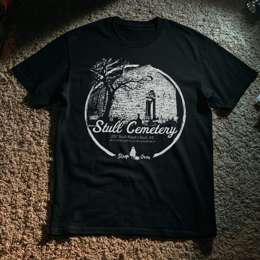 Black T-shirt with a white illustration of the crumbling church ruins at Stull Cemetery in Stull, Kansas—rumored to be one of the seven gateways to hell. Includes the address and coordinates with Sleep Over ghost branding below.